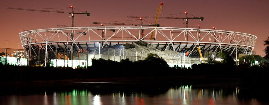 gran estructura estadio fútbol en construcción con grúas visibles en primer plano un río